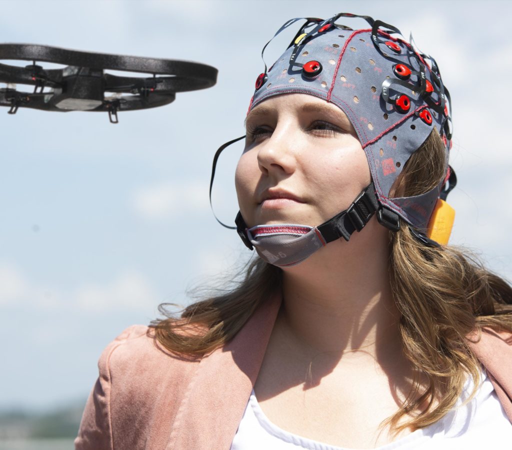 A woman wearing a special headpiece with sensors, flying a drone