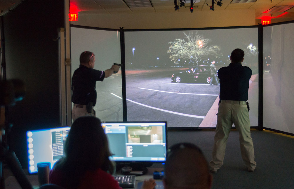 two police officers use a virtual reality simulation while observers record their movements