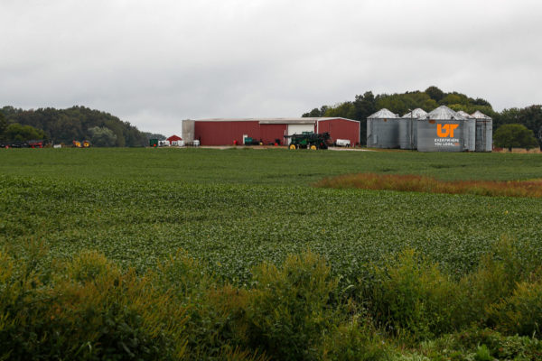 A red barn and a group of grain silos in a green agricultural field. One one of the silos has the UT icon painted on it