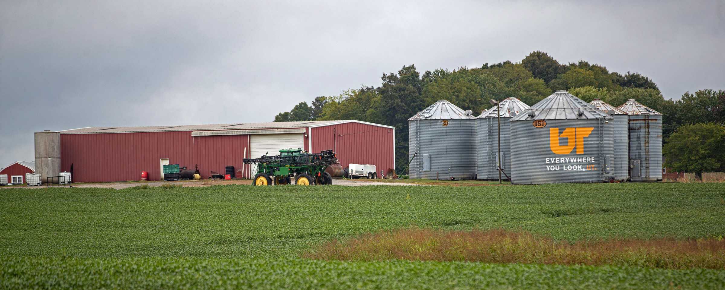 A red barn and a group of grain silos in a green agricultural field. One one of the silos has a large UT icon painted on it