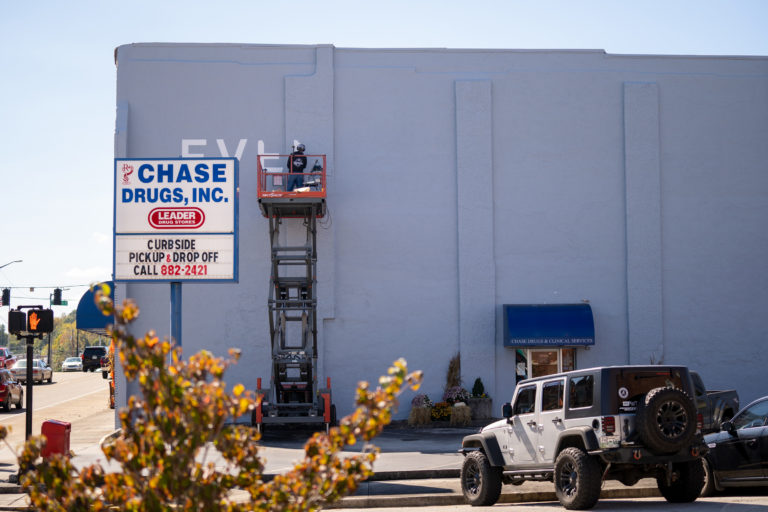 artist Troy Freeman paints letters on the Chase pharmacy building from a lifted platform bed