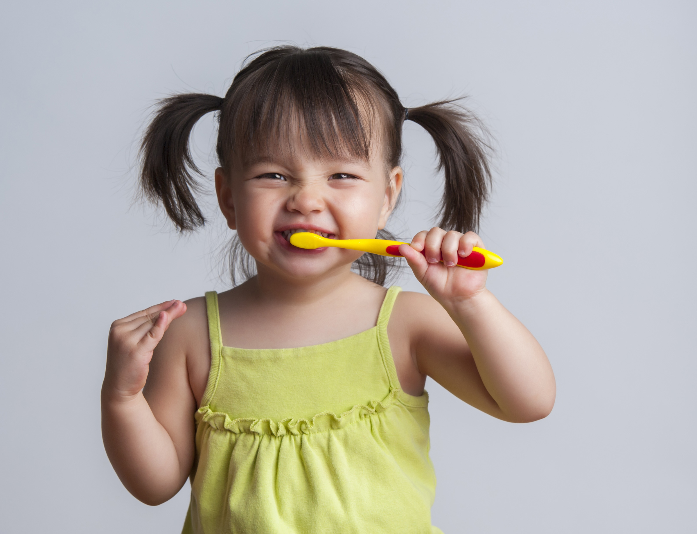 A young girl brushes her teeth with a kid sized toothbrush