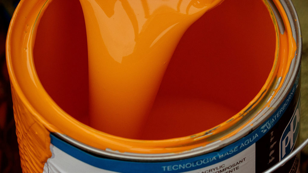 Orange paint pouring into a paint can