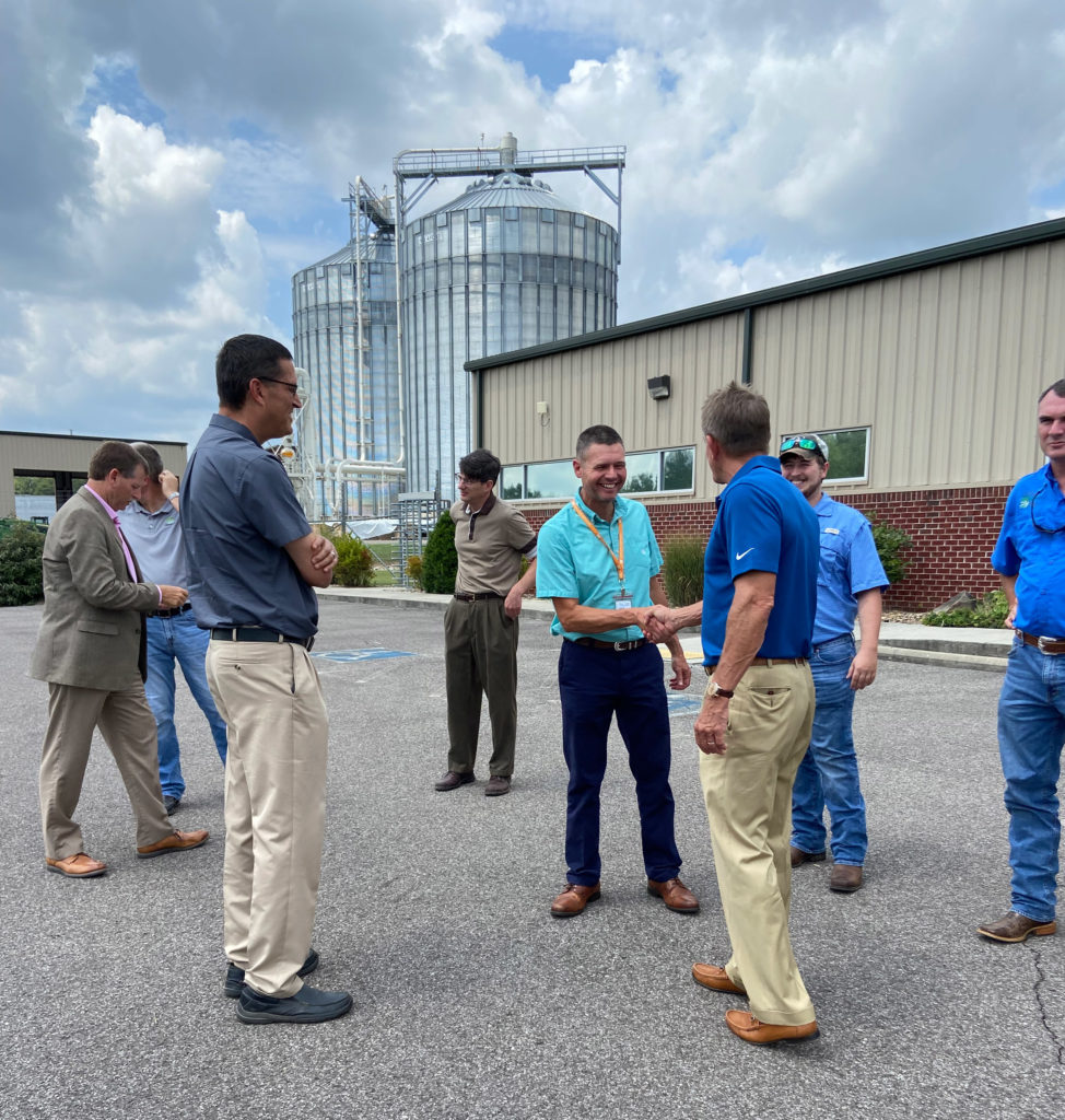 Randy Boyd shakes hands with Genera employees outside the plant. Two large storage silos can be seen in the background