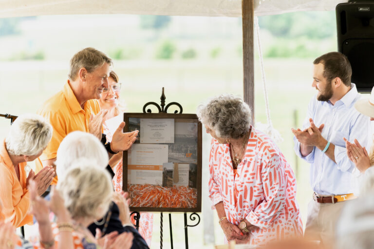 UT President Randy Boyd clapping as Rena Johnson accepts a token of appreciation from UT during the mural dedication ceremony at Johnson Farm held May 26, 2023