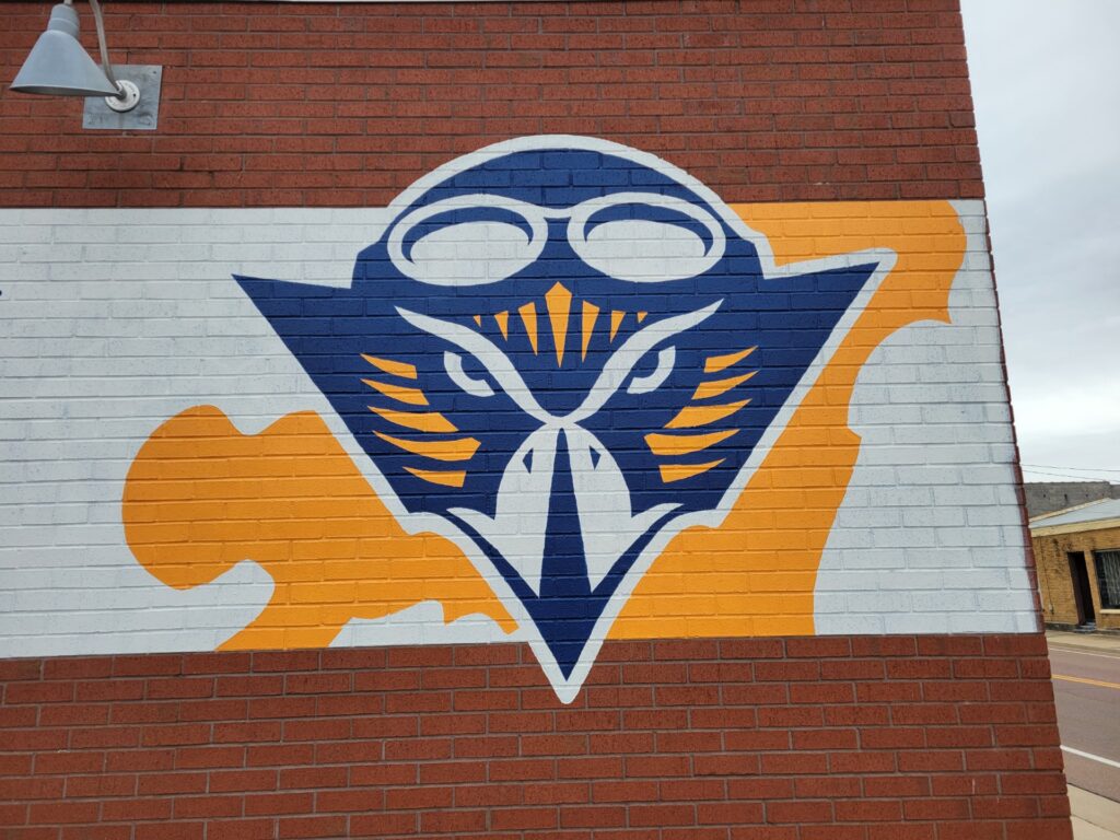 Orange, white and blue mural of UT Martin Skyhawk painted on red brick