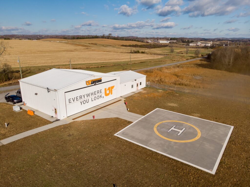 Aerial photo of gray and orange "Everywhere You Look, UT" mural painted on white helicopter hangar in Sweetwater, Tennessee