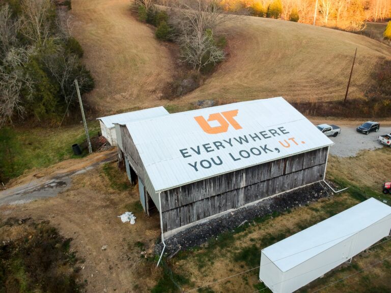 Aerial view of orange and gray "Everywhere You Look, UT" mural painted on white barn roof