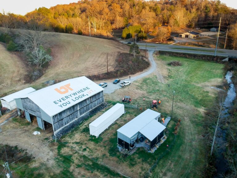 Aerial view of orange and gray "Everywhere You Look, UT" mural painted on white barn roof in Strawberry Plains