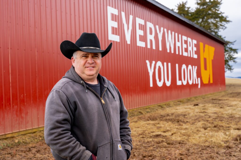 Whitt Shuford, operator of Fugate Farms in Tazwell, Tennessee, stands in front of red barn painted with "Everywhere You Look, UT" slogan