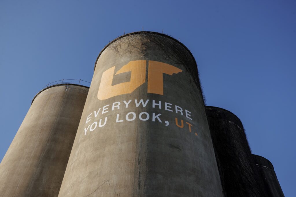 Photo looking up at concrete silos painted with orange and white Everywhere You Look, UT mural