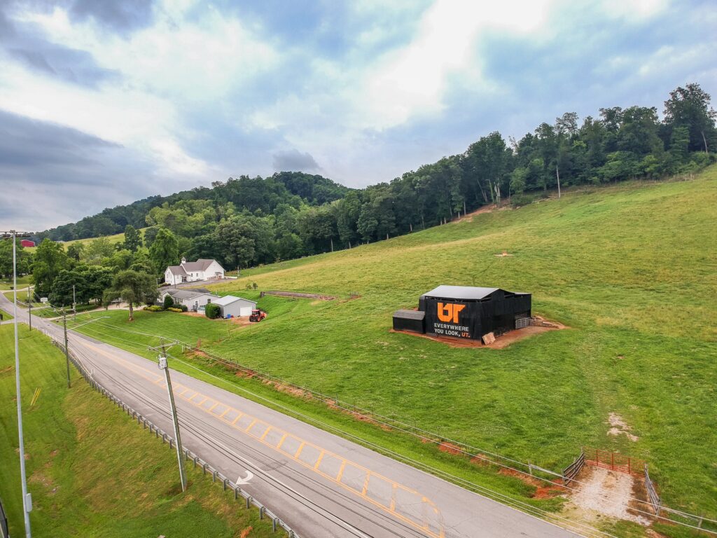 Aerial view of orange and white Everywhere You Look, UT mural painted on black barn overlooking highway