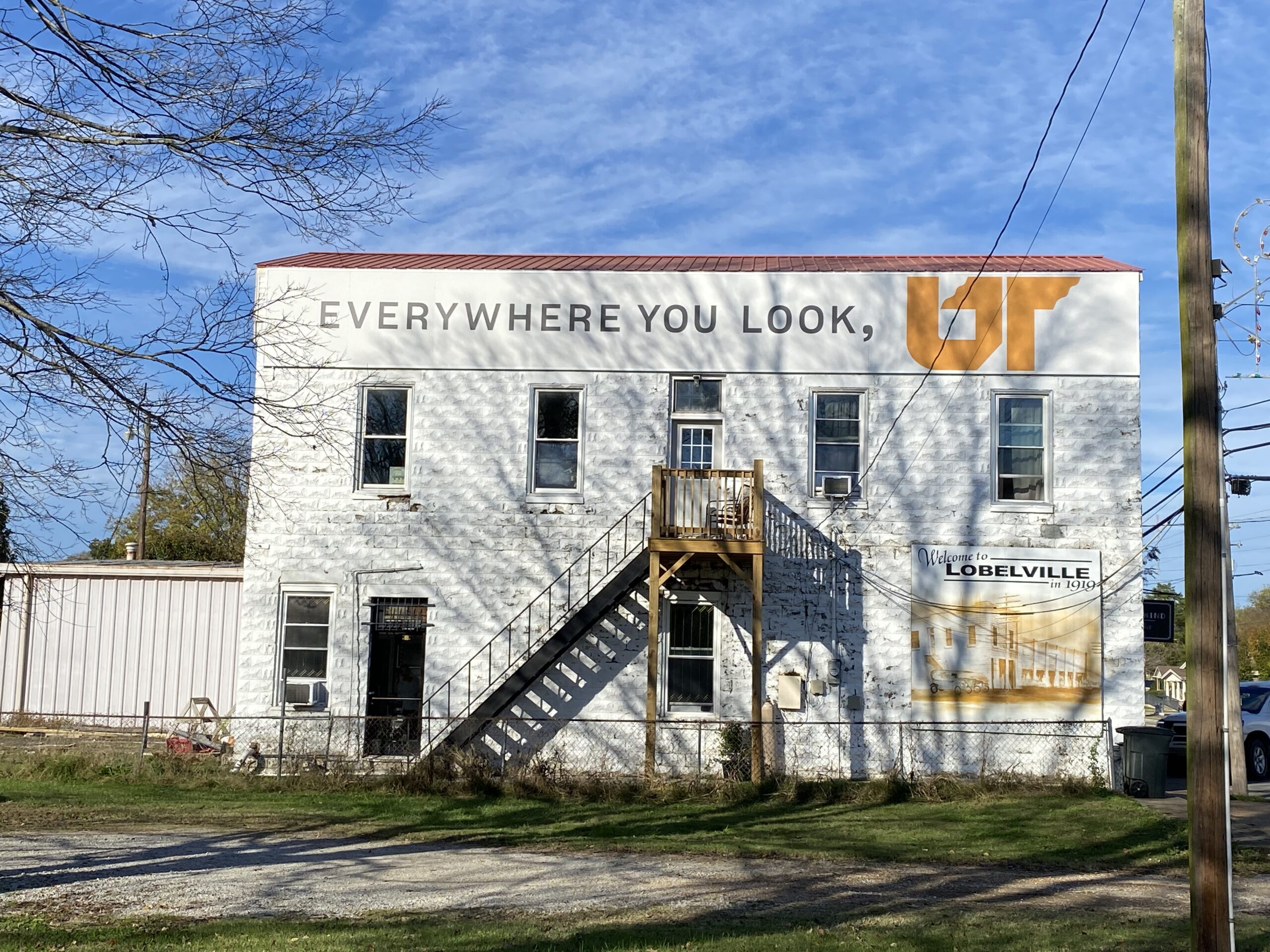 Gray and white Everywhere You Look, UT mural along roofline of historic bank in Lobelville, Tennessee