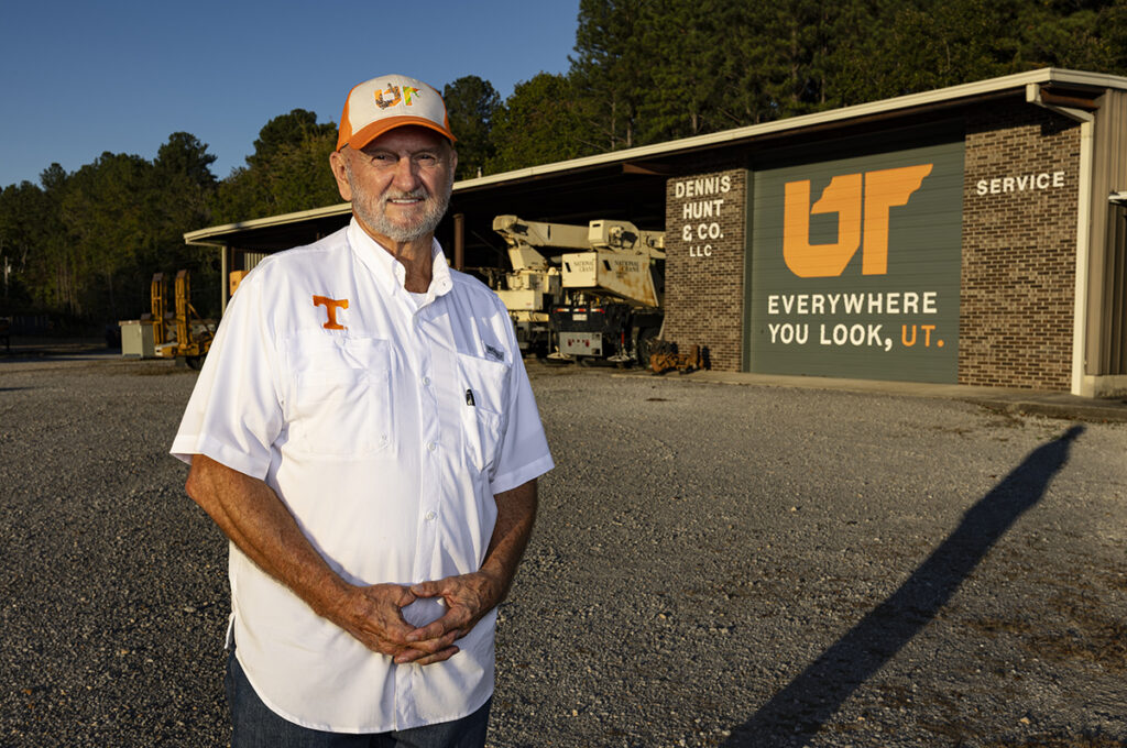 Man in a white shirt standing next to a brick building with a painted mural.