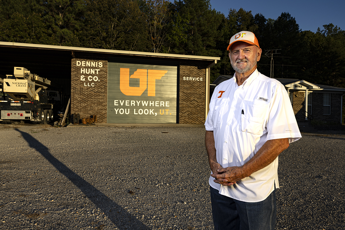 Man in a white shirt standing next to a brick building with a painted mural.