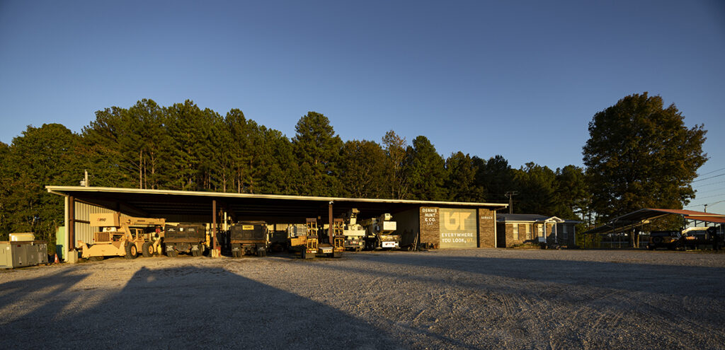 Small brick building with metal roofing and construction vehicles parked underneath.
